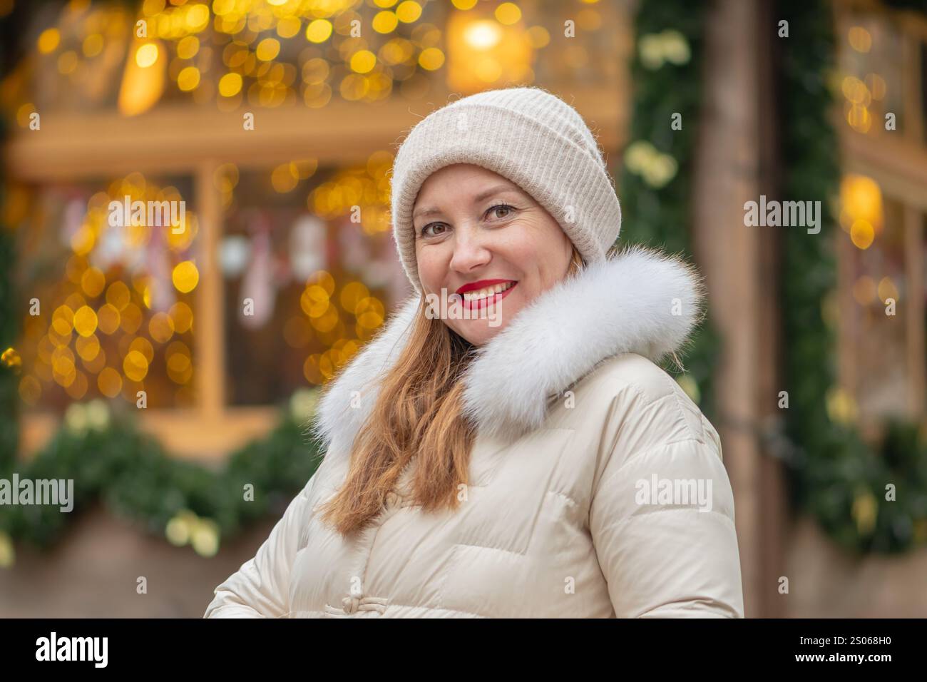 Lächelnde Frau 30-35 Jahre alt auf dem Hintergrund farbenfroher Lichter von Girlanden während der Feiertage in einer der Städte. Stockfoto