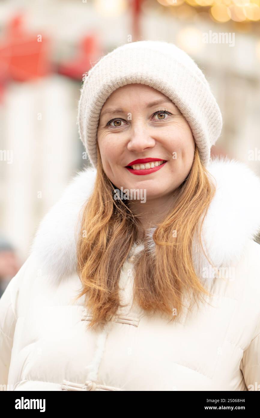 Lächelnde Frau 30-35 Jahre alt auf dem Hintergrund farbenfroher Lichter von Girlanden während der Feiertage in einer der Städte. Stockfoto