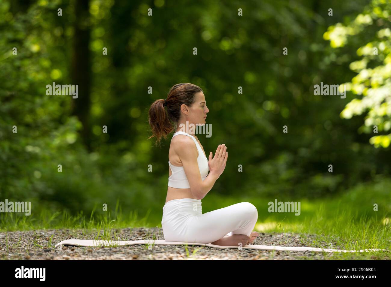 Frau sitzend im Kreuzbein meditierend und im Park Yoga praktizierend Stockfoto