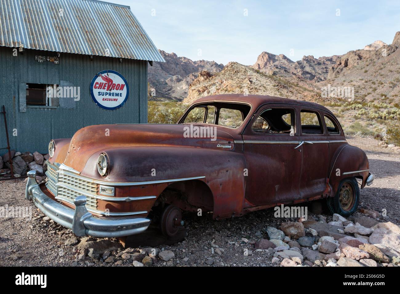 Ein verrostetes altes Auto steht vor einem Gebäude mit einem blauen Schild mit der Aufschrift 'Chevron' Stockfoto