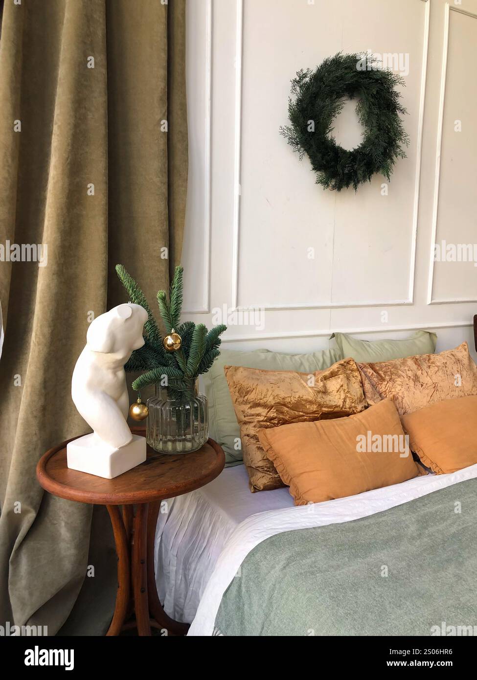 Diese elegante, im Winterstil gestaltete Schlafzimmerecke bietet eine harmonische Mischung aus Erdtönen und minimalistischer Einrichtung. Ein grüner Kranz hängt an der weißen Verkleidung Stockfoto