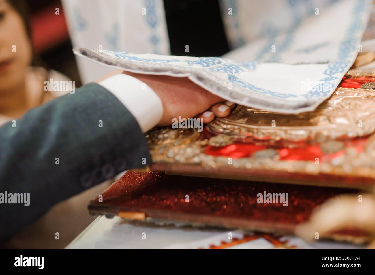 Eine Nahaufnahme einer Hand, die während einer Zeremonie eine religiöse Ikone auf eine kunstvolle Oberfläche legt. Stockfoto