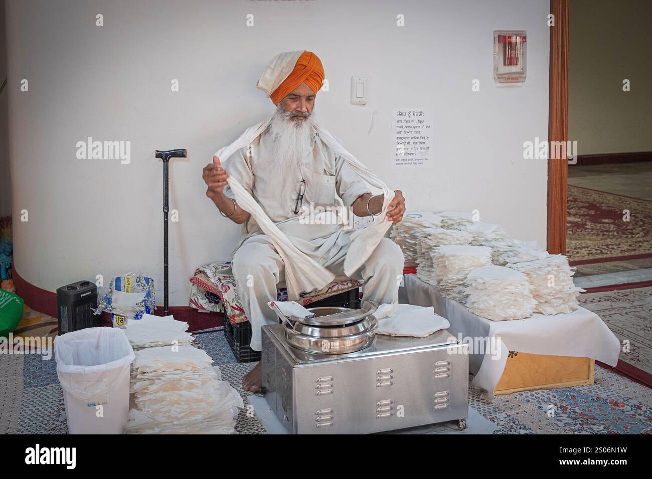 Ein Sikh-Ältester in weißen Gewändern macht sich bereit, Karah prasad an Anbeter zu verteilen. Es ist symbolisch für Gottes Gnade. In einem Tempel in Queens, NY. Stockfoto