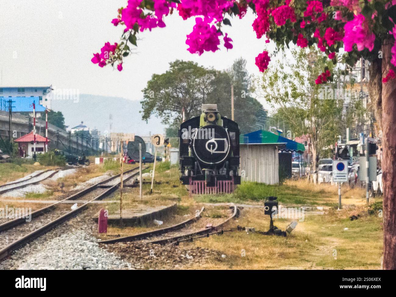 Am Bahnhof Hua hin hängen Pflanzen mit hübschen und lebendigen Blüten, im späten Nachmittagslicht, die eine alte, stillgelegte Dampflokomotive BE umrahmen Stockfoto