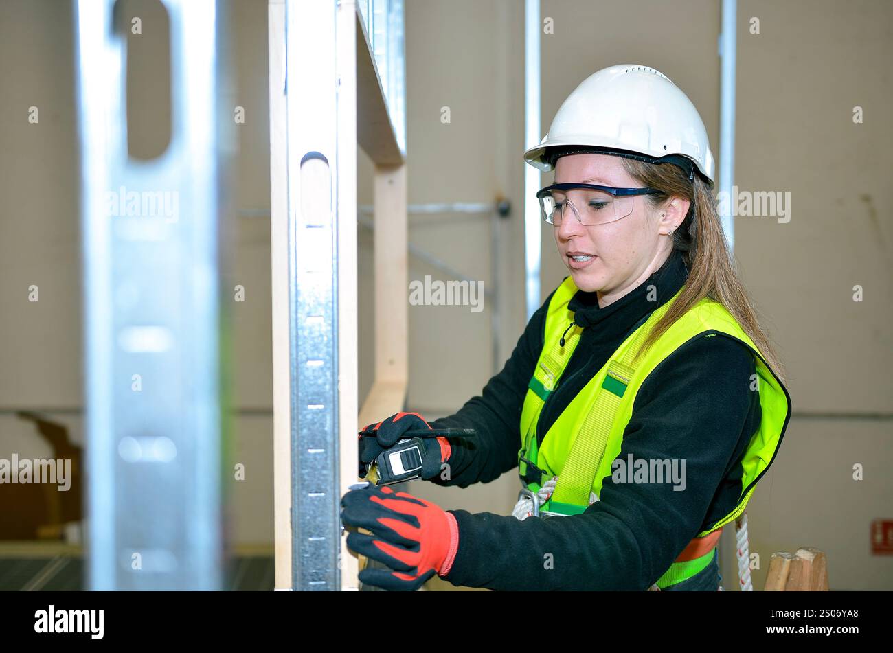 Bauarbeiterin, die Gipskartonplatten mit einem Laser-Entfernungsmesser misst, um eine präzise Installation während des Bauprozesses zu gewährleisten Stockfoto