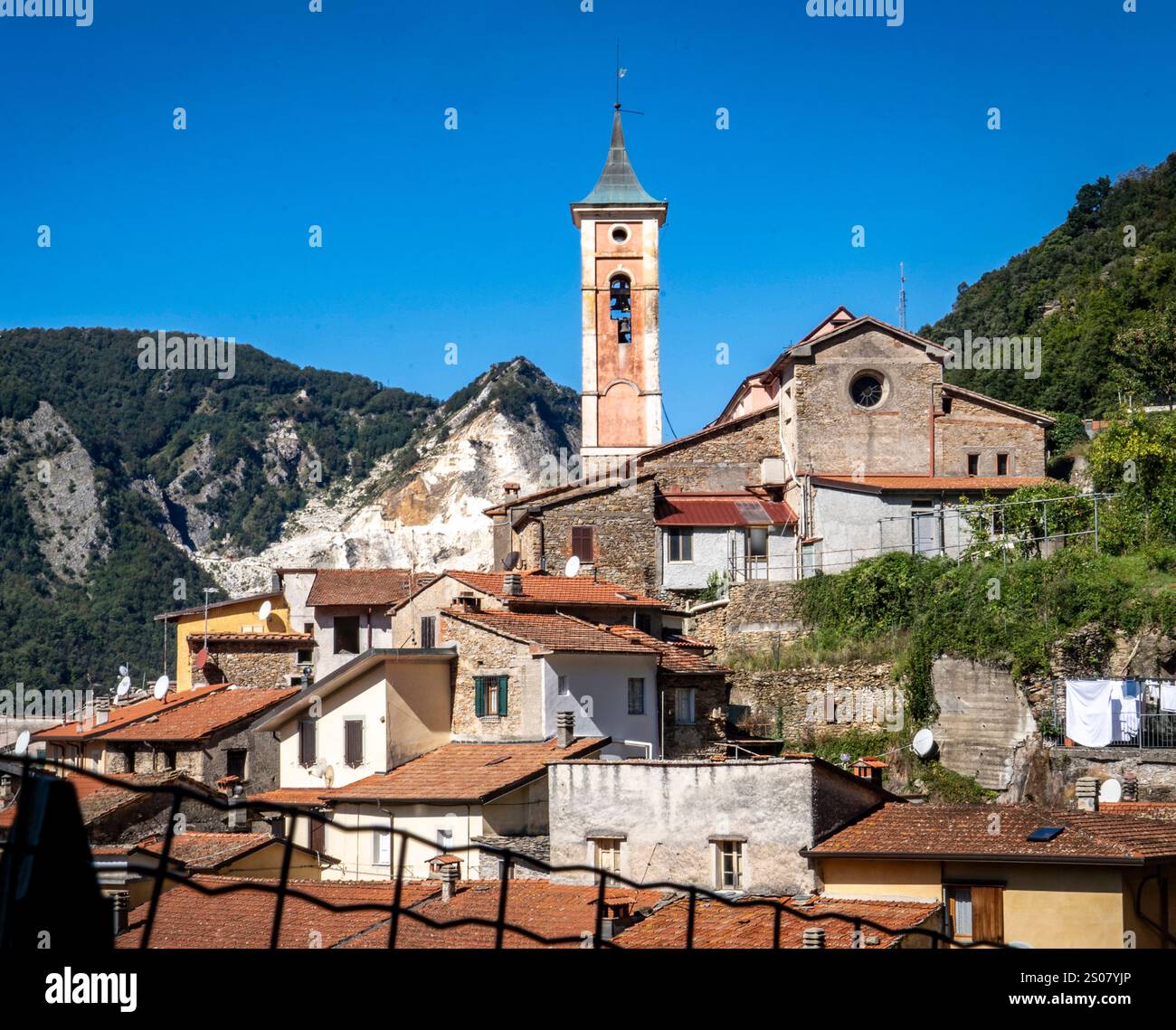 Ein malerischer Blick auf ein kleines italienisches Dorf mit traditioneller Architektur, mit einem hohen Uhrenturm und Bergen im Hintergrund. Stockfoto