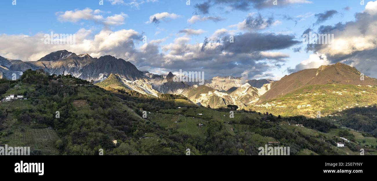 Ein Panoramablick auf eine bergige Landschaft unter teilweise bewölktem Himmel. Im Vordergrund befinden sich üppige grüne Hügel mit Bäumen und kleinen weißen Bäumen Stockfoto