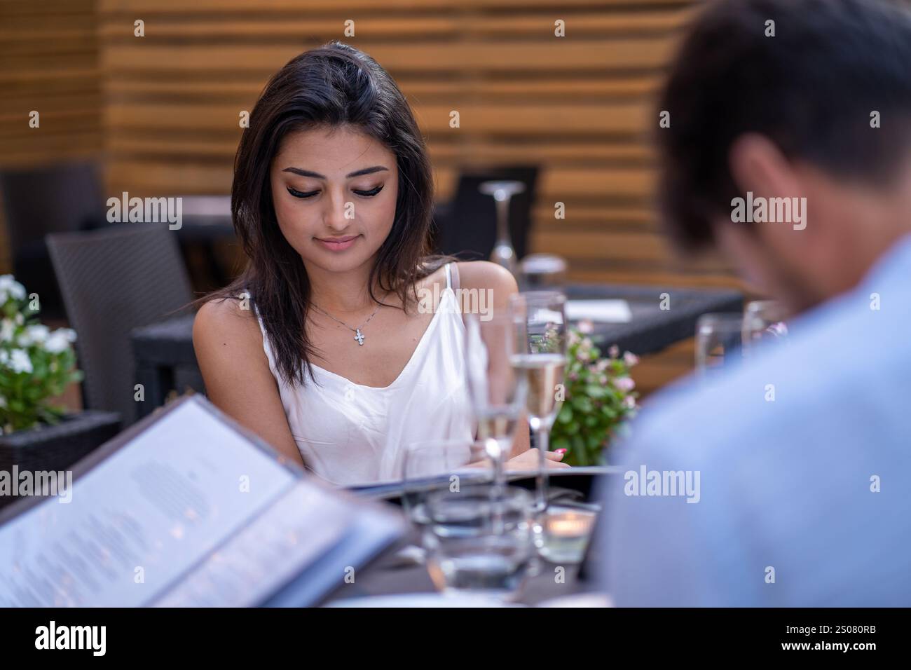 Konzentrierte junge Frau, die ein Menü an einem Tisch im Freien liest, umgeben von einer entspannten und stilvollen Atmosphäre. Stockfoto