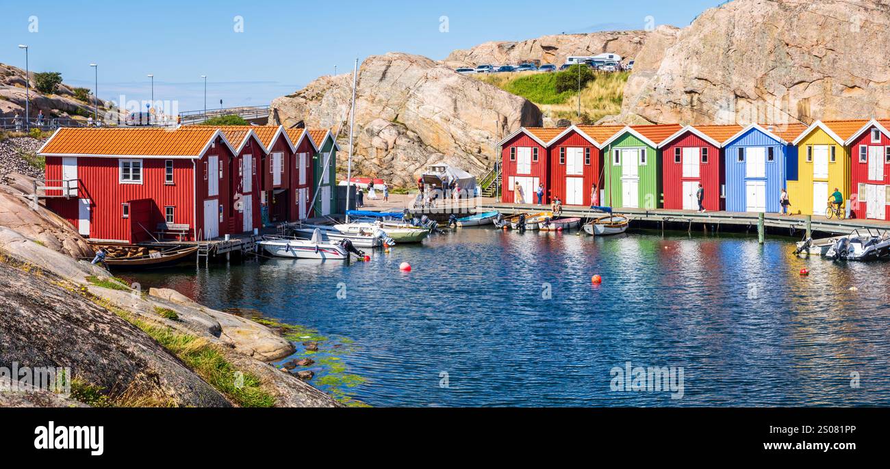 Panoramablick auf farbenfrohe hölzerne Bootshäuser, die sich an einem sonnigen Sommertag an der felsigen Klippe entlang des Meereskanals in Smögen, Schweden, aneinanderreihen. Stockfoto