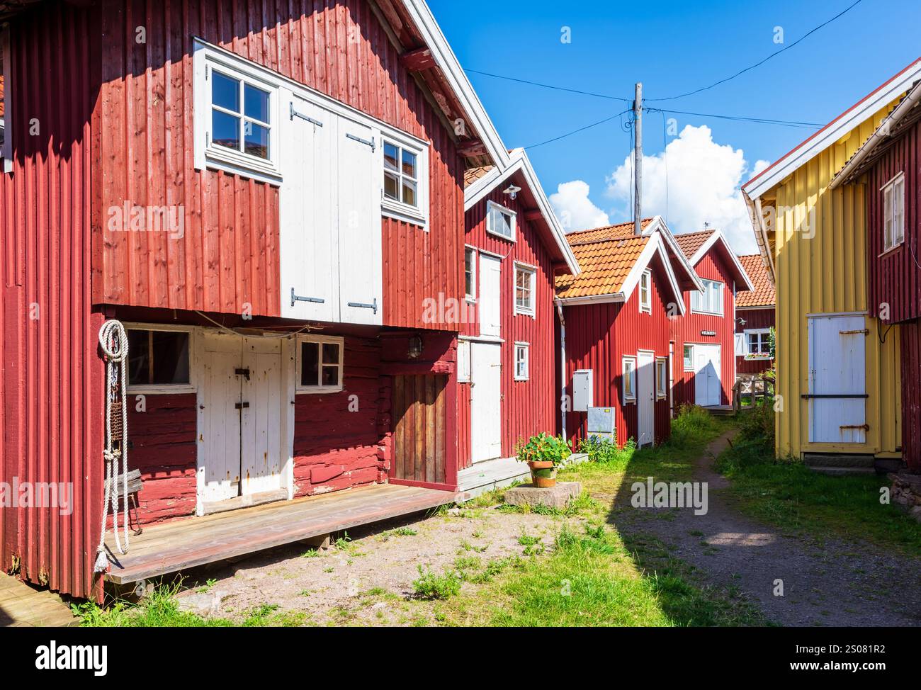 An einem sonnigen Sommertag Reihen sich alte rot bemalte Holzhäuser entlang einer grasbewachsenen Gasse im historischen Zentrum von Smögen, Schweden. Stockfoto