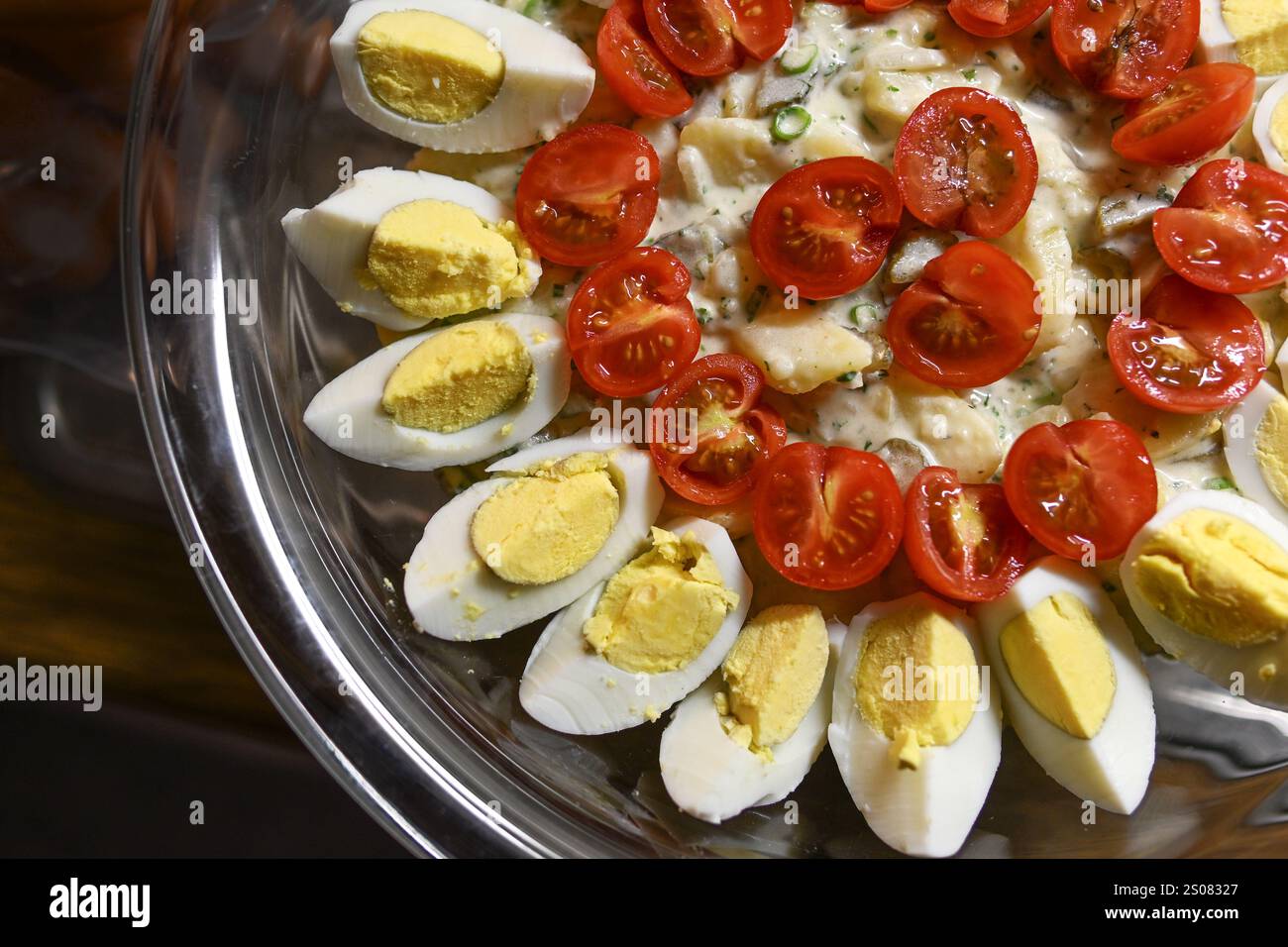 Teil eines Kartoffelsalats mit gekochten Eiern und Cocktailtomaten als Garnitur in einer Glasschale, Blick von oben, Kochen für ein Partybuffet oder eine Familie Stockfoto