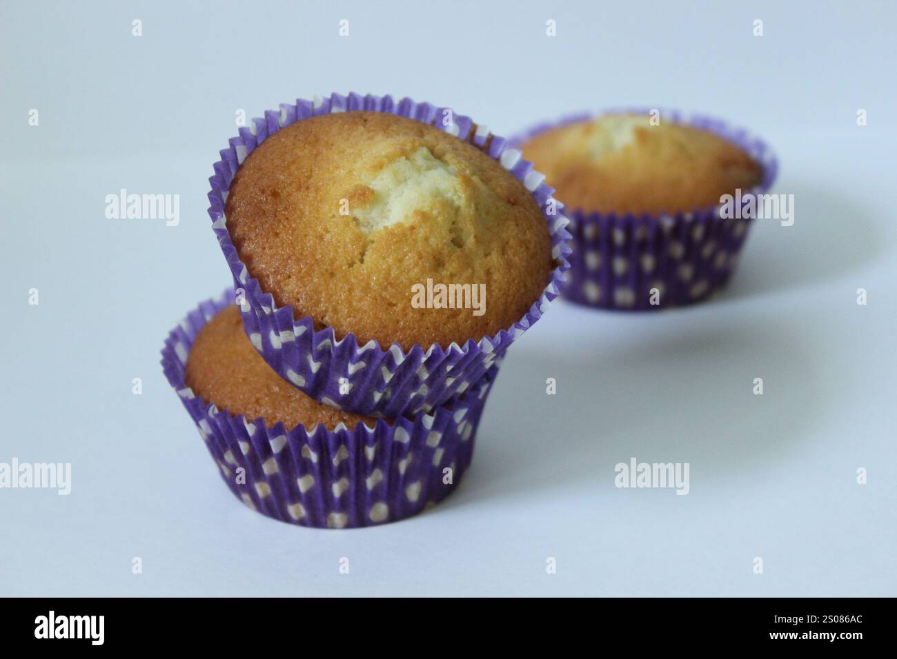 Drei goldene Muffins, eingebettet in leuchtend violette Pappbecher, schaffen ein verführerisches Arrangement Stockfoto