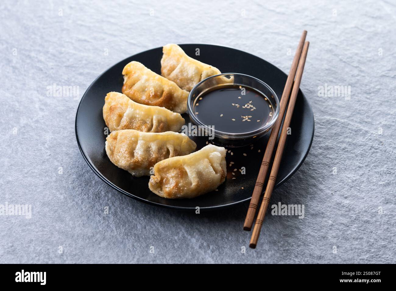 Gebratene Knödel Gyoza mit Sojasauce auf grauem Steingrund Stockfoto