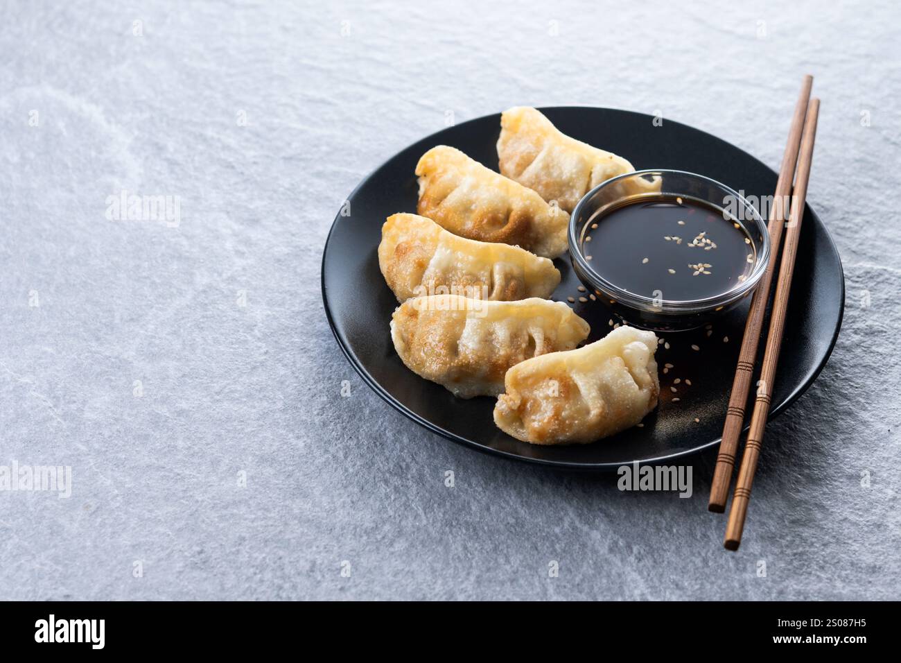 Gebratene Knödel Gyoza mit Sojasauce auf grauem Steingrund Stockfoto