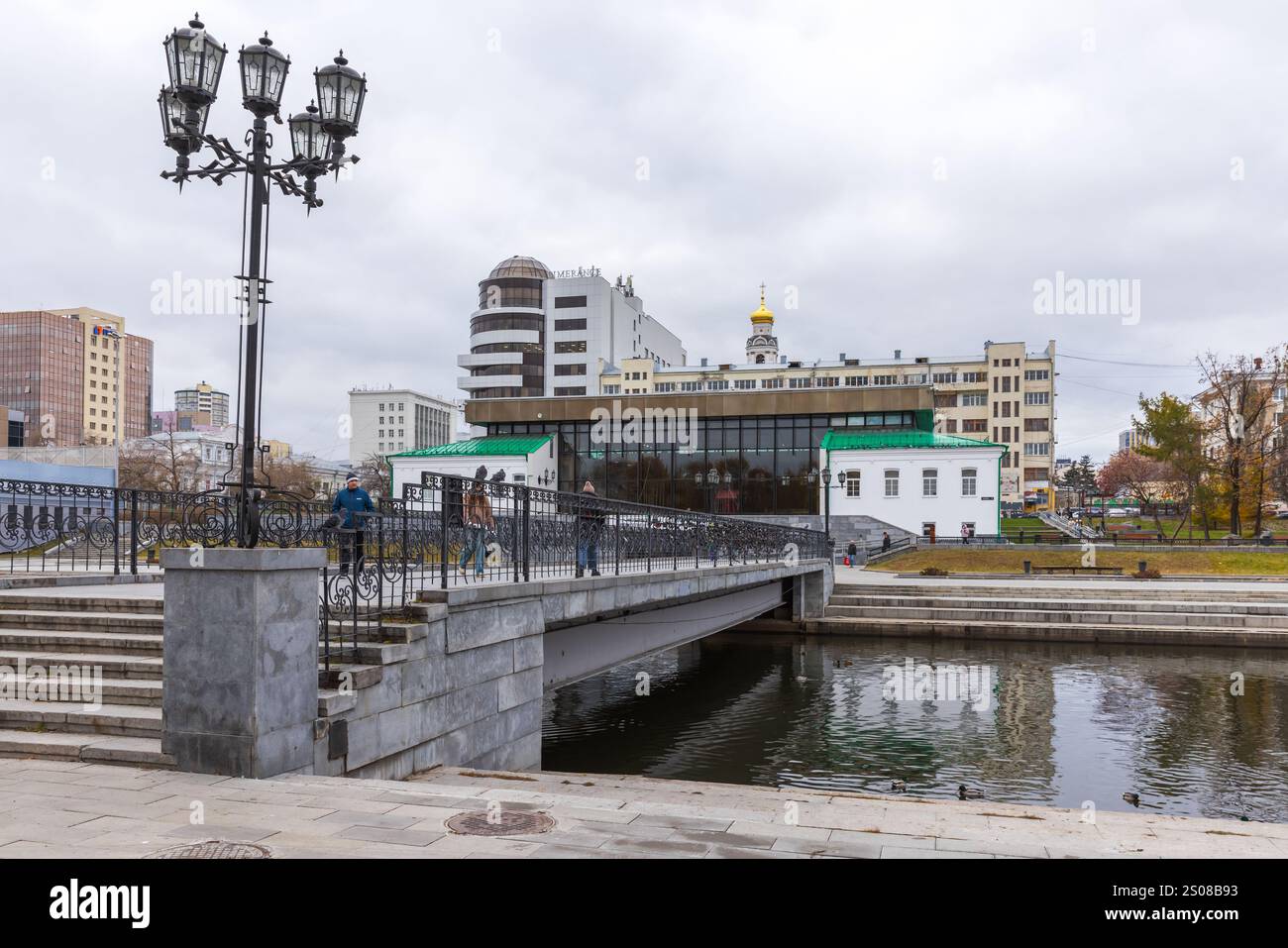 Jekaterinburg, Russland - 25. Oktober 2024: Stadtbild mit Fußgängerbrücke über den Fluss Iset. Die Leute gehen am Ufer entlang Stockfoto