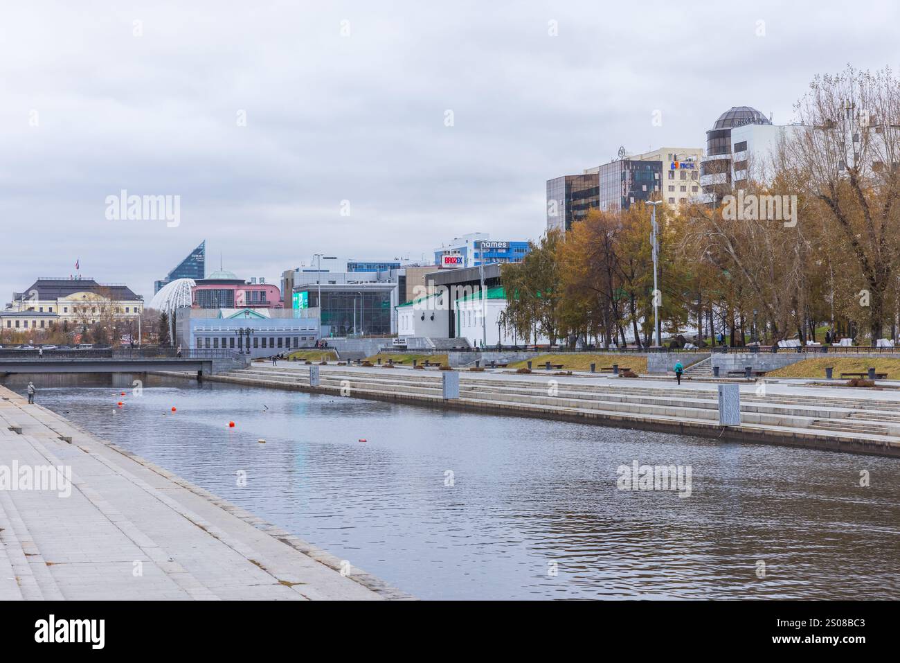 Jekaterinburg, Russland - 25. Oktober 2024: Stadtbild mit dem Fluss Iset. Die Leute gehen am Ufer entlang. Das Museum der Schönen Künste befindet sich im Hintergrund Stockfoto