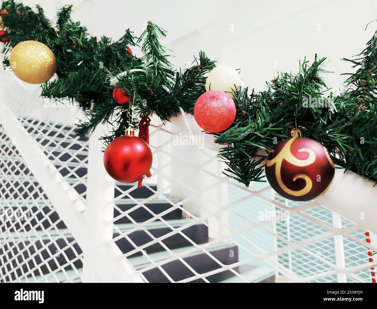 Bunte Weihnachtskugeln hängen an einer Girlande am Geländer und schaffen eine festliche Atmosphäre. Die Dekorationen haben verschiedene Designs und fügen V Stockfoto