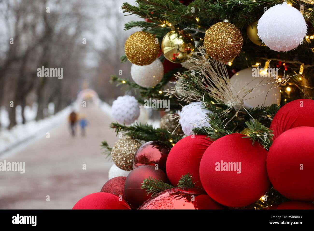Neujahrsfeier in der Winterstadt, Weihnachtsbaumzweige mit roten und goldenen Kugeln auf Parkhintergrund Stockfoto