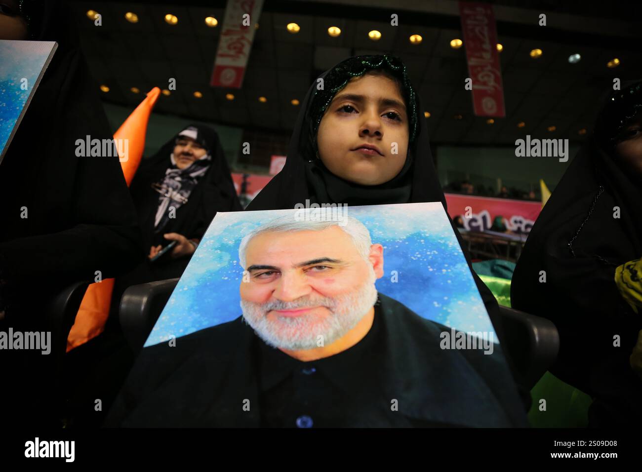 Teheran, Iran. Dezember 2024. Ein iranisches junges verschleiertes Mädchen trägt ein Porträt von Generalmajor Qasem Soleimani, der bei einem US-Drohnenangriff in Bagdad am 3. Januar 2020 während seiner Jubiläumsfeier im Azadi Indoor Stadium im Westen Teherans getötet wurde. (Kreditbild: © Rouzbeh Fouladi/ZUMA Press Wire) NUR REDAKTIONELLE VERWENDUNG! Nicht für kommerzielle ZWECKE! Stockfoto