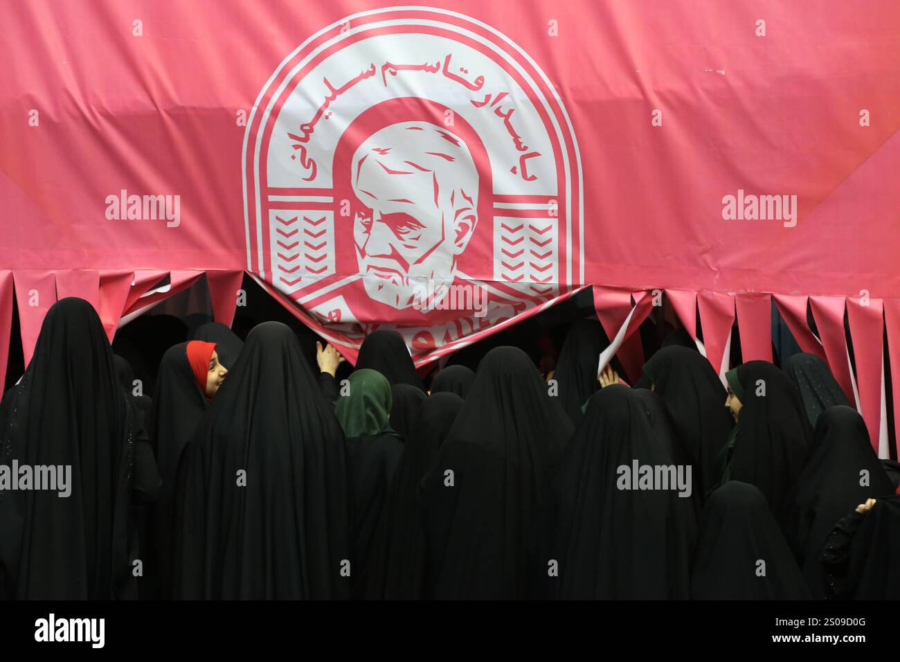 Teheran, Iran. Dezember 2024. Iranische verschleierte Schulmädchen laufen unter einem Porträt von Generalmajor Qasem Soleimani, der bei einem US-Drohnenangriff in Bagdad am 3. Januar 2020 während seiner Jubiläumsfeier im Azadi Indoor Stadium im Westen Teherans getötet wurde. (Kreditbild: © Rouzbeh Fouladi/ZUMA Press Wire) NUR REDAKTIONELLE VERWENDUNG! Nicht für kommerzielle ZWECKE! Stockfoto