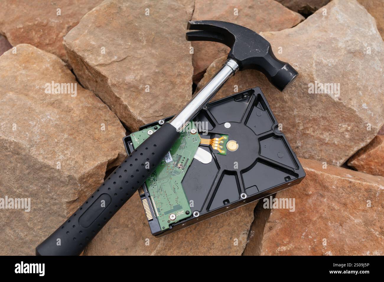 Hammer liegt auf alter Festplatte auf Steinen, Konzept auf garantierter Datenvernichtung, alte Technologien Stockfoto