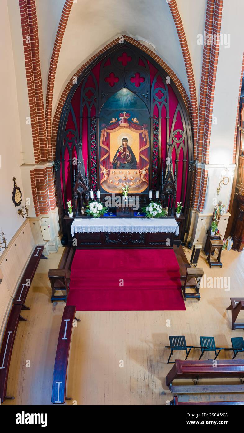 Das Bild zeigt ein Kircheninnere mit einem reich verzierten Altar mit einer religiösen Ikone, Blumenarrangements und Kerzen im gotischen Stil Stockfoto