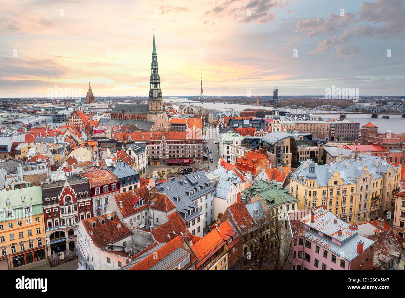 Rigas historische Architektur mit farbenfrohen Gebäuden und roten Ziegeldächern. Der Turm der Peterskirche und der Rigaer Fernsehturm zeichnen sich durch einen Sonnenuntergang aus. Stockfoto