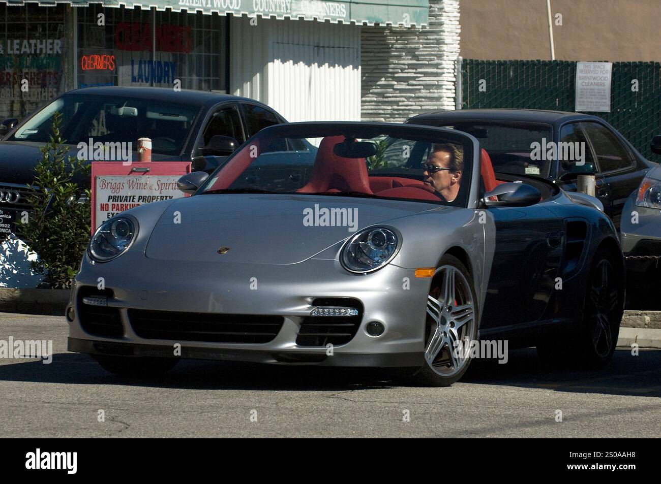 Arnold Schwarzenegger ging lässig in einem weißen T-Shirt und Shorts, später fuhr er ein silbernes Porsche-Cabrio mit roter Innenausstattung. Brentwood, CA. Stockfoto