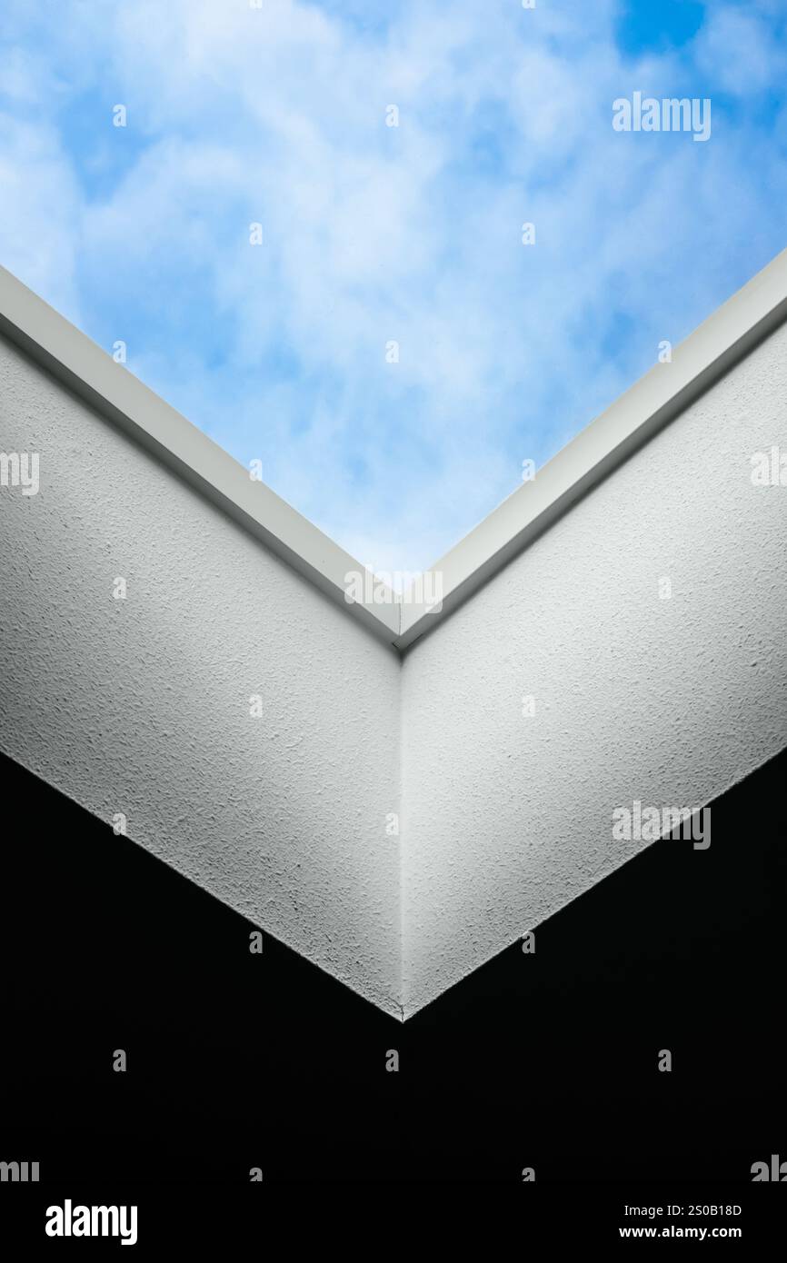 Geometrie des Oberlichts. Blauer Himmel mit flauschigen weißen Wolken zeigt sich durch ein weißes Oberlicht. Der Blickwinkel erzeugt eine Illusion des Himmels in einem Kasten. Stockfoto