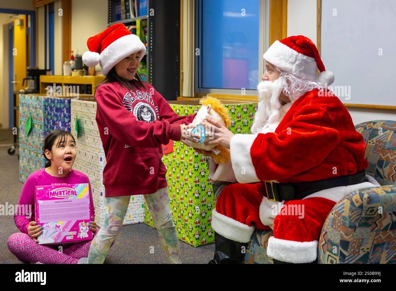 Kotzebue, Alaska, USA. Dezember 2024. Kapitän Michael McDonald, gekleidet als Weihnachtsmann, übergibt einem Schüler ein Spielzeug an der June Nelson Elementary School in Kotzebue, Alaska, 5. Dezember 2024. McDonald, Inspektor und Ausbilder der Detachment Delta Company, 4. Strafverfolgungsbataillon, Force Headquarters Group, Marine Forces Reserve, zusammen mit Mitgliedern der Air Force und Navy, verteilte Spielzeug an lokale Schulkinder während der diesjährigen Toys for Tots Operation. Die Toys for Tots-Mission ist ein Beispiel für den Geist des Marine Corps in The Last Frontier und stärkt die Gemeindebeziehungen und schärft gleichzeitig Stockfoto