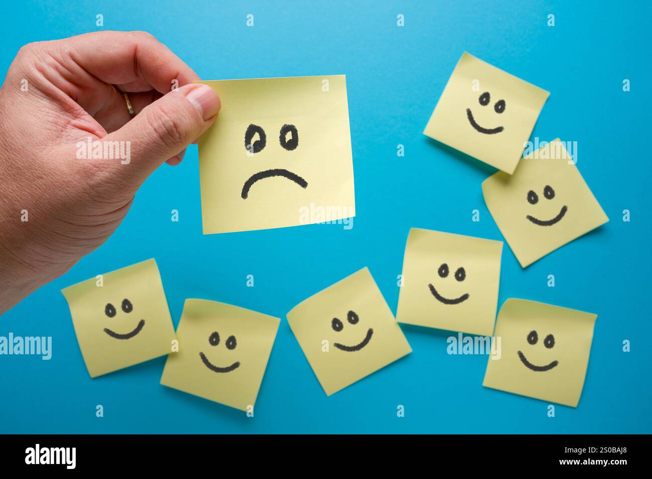 Haftnotizpapier mit einem traurigen Gesichtssymbol, umgeben von Smiley-Gesichtern Stockfoto