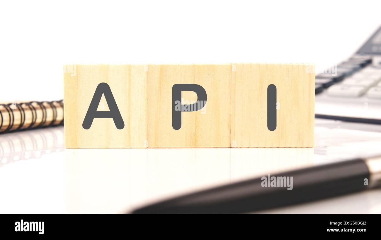 API-Abkürzung, modernes Technologiekonzept. API es ist auf Holzwürfeln in einer Komposition mit Taschenrechner, Stift, Notizbuch auf weißem Hintergrund geschrieben Stockfoto