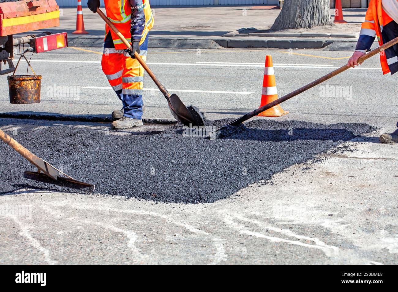 Straßenarbeiter reparieren an einem sonnigen Tag den Straßenbelag mit leuchtend orangefarbenen Kegeln, die die Baustelle markieren Stockfoto