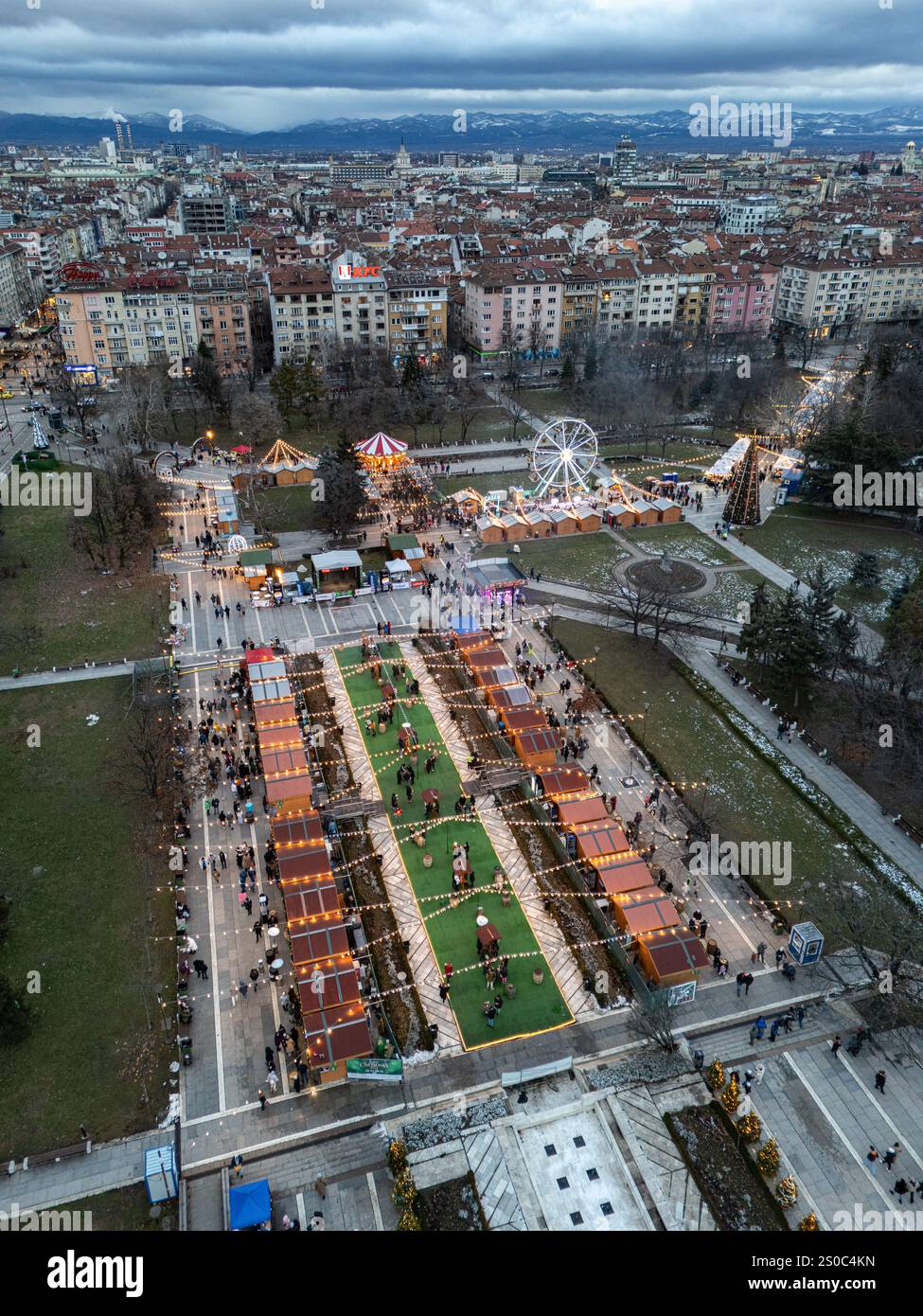 Ein lebhafter Blick aus der Vogelperspektive auf Sofias Weihnachtsmarkt in der Nähe des Nationalen Kulturpalastes (NDK). Festliche Lichter, Riesenrad und winterlicher Charme. Stockfoto