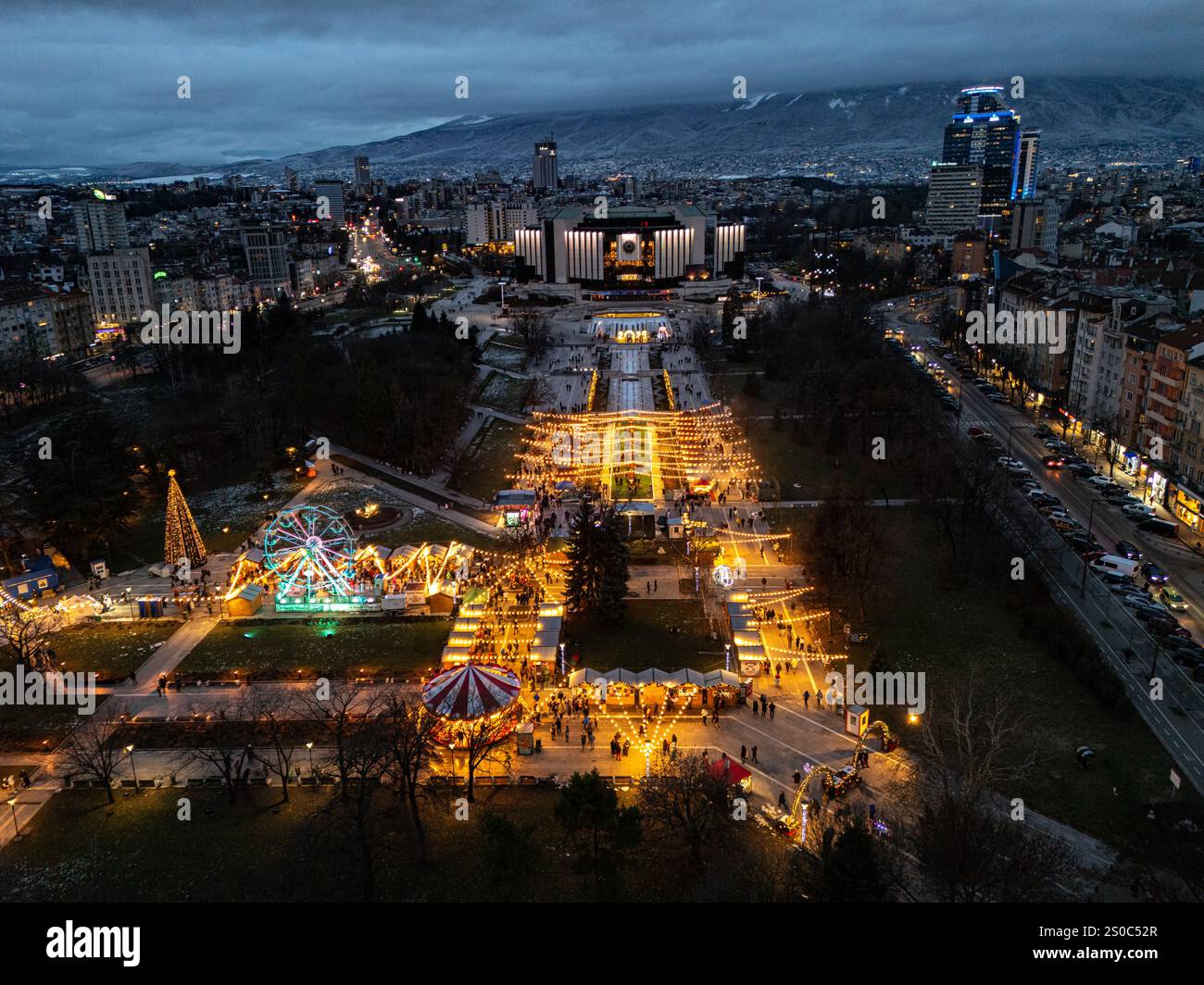 Luftaufnahme des Nationalen Kulturpalastes (NDK) in Sofia, Bulgarien, mit beleuchtetem Weihnachtsmarkt mit Riesenrad und festlichen Lichtern. Stockfoto