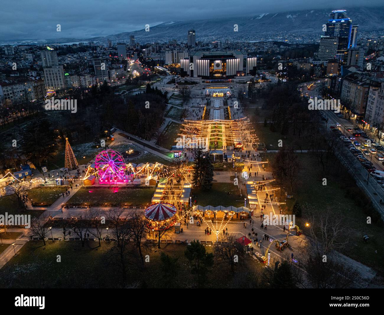 Luftaufnahme des Nationalen Kulturpalastes (NDK) in Sofia, Bulgarien, mit beleuchtetem Weihnachtsmarkt mit Riesenrad und festlichen Lichtern. Stockfoto