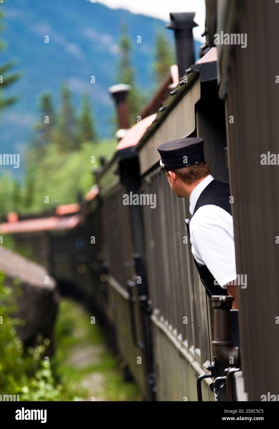 Skagway Alaska, Zugbegleiter der White Pass and Yukon Route Railway, beugt sich zwischen den Autos und bietet eine bessere Aussicht. Stockfoto