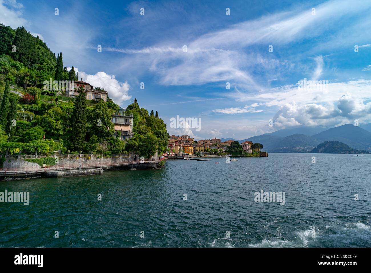 Ein malerisches Dorf am See mit farbenfrohen Häusern, üppigem Grün und atemberaubendem Blick auf die Berge unter einem hellblauen Himmel, das die ruhige Schönheit und widerspiegelt Stockfoto