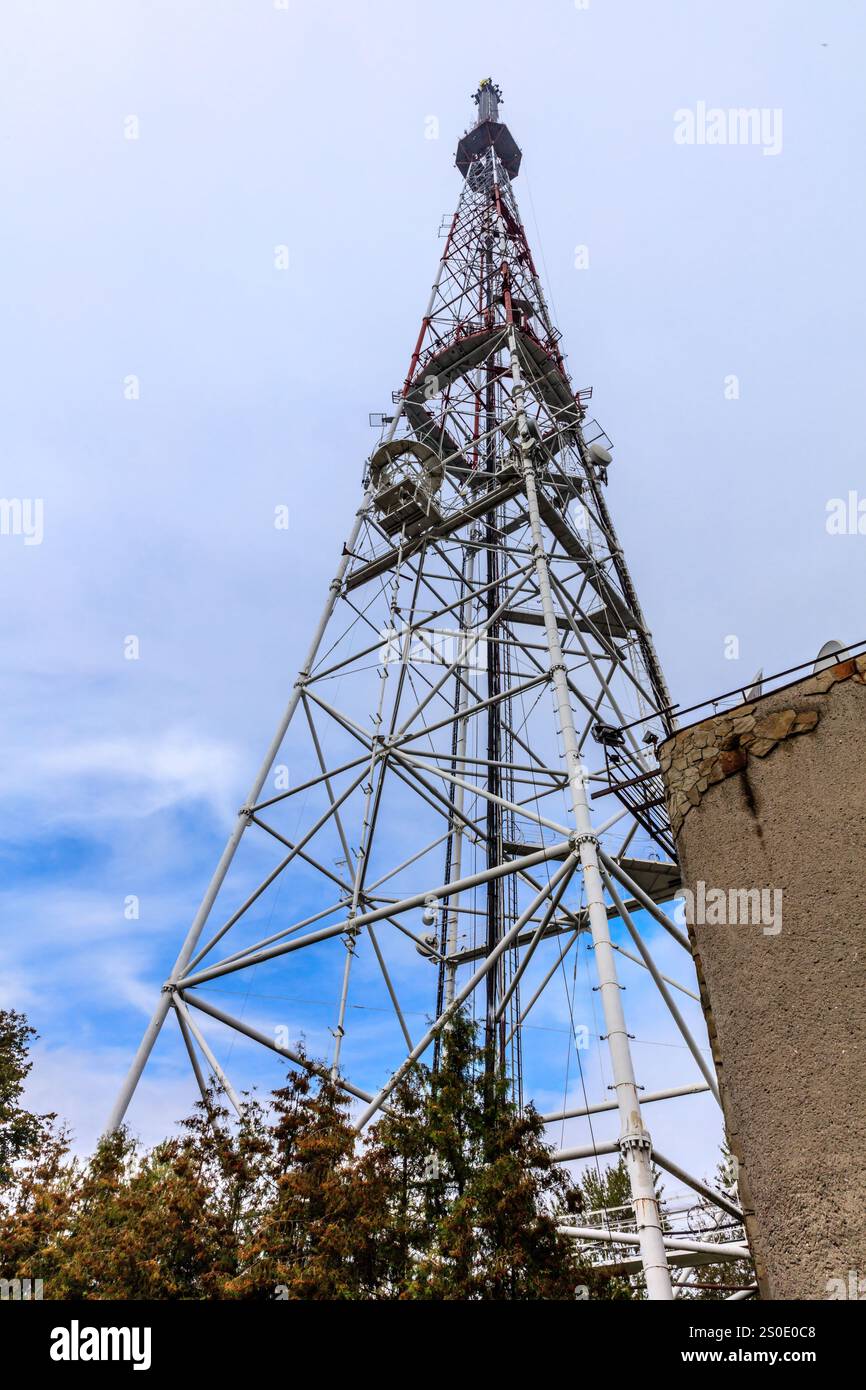 Ein hoher Turm mit roter Spitze und weißem Sockel. Der Turm ist von Bäumen umgeben und liegt an einem bewölkten Himmel Stockfoto