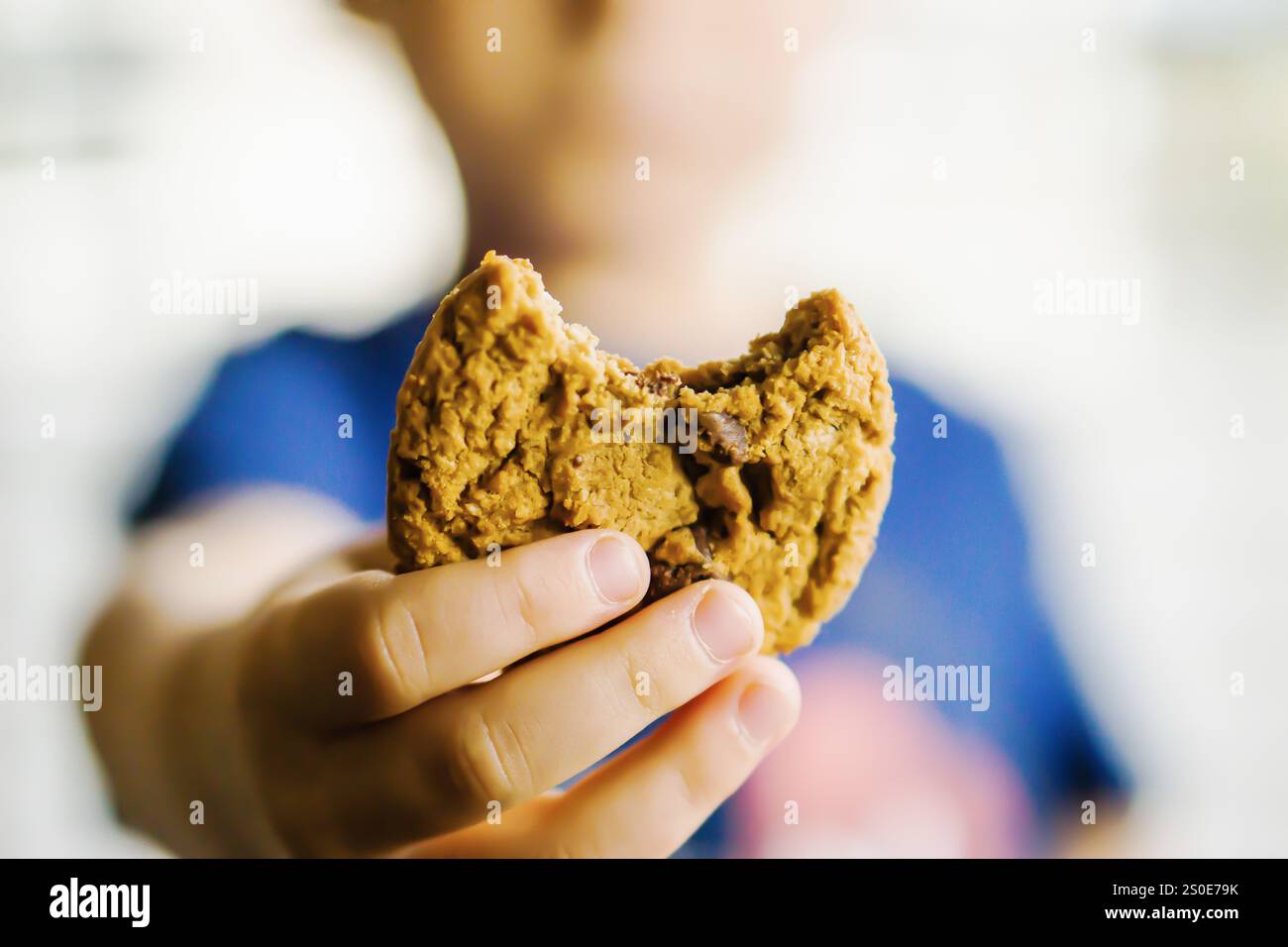 Ein Kind hält einen Keks in der Hand, und ein Biss wird daraus entfernt. Das Konzept der Unschuld und des Genusses, da das Kind eine süße Leckerei genießt Stockfoto