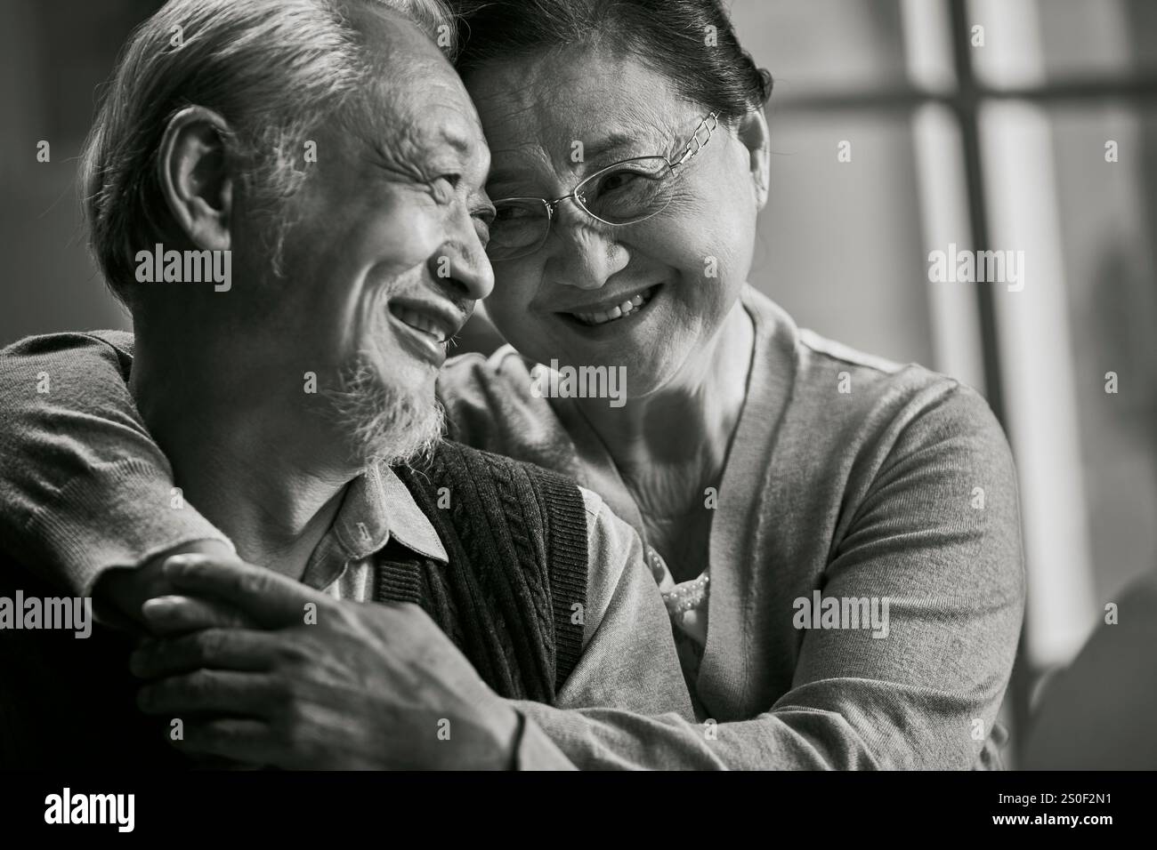 Schwarz-weiß-Porträt eines glücklichen liebenden älteren asiatischen Paares, das zu Hause auf der Couch sitzt Stockfoto