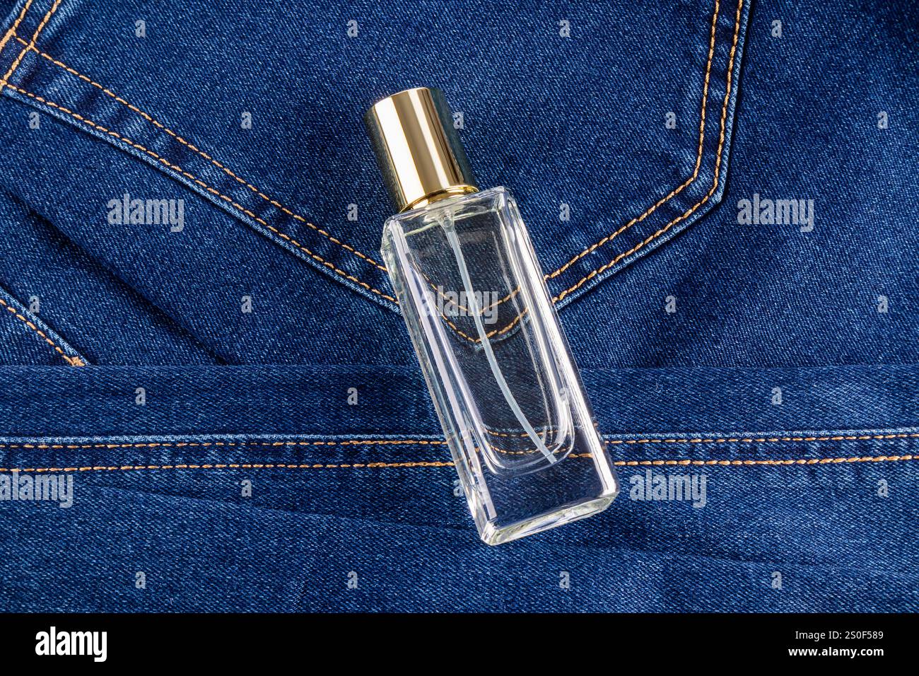 Eine stilvolle, transparente Flasche Parfüm für Herren liegt auf einer blauen Jeans. Draufsicht. Ansicht schließen. Makro. Ein leeres Flaschenmodell. Duftpräsentation Stockfoto