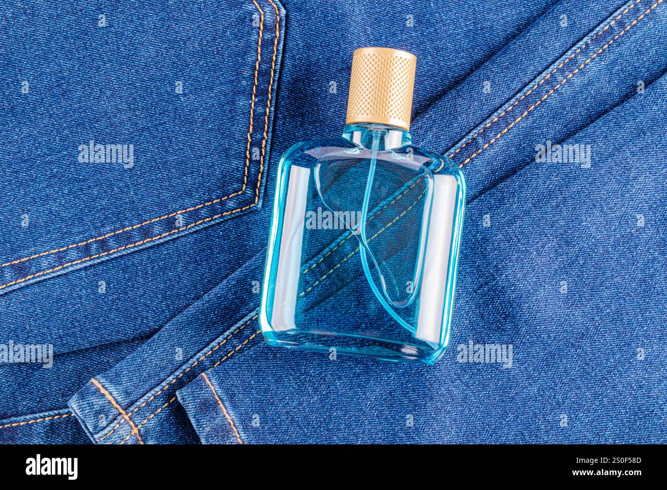 Transparente Flasche mit blauem Parfüm Männerflüssigkeit, Gesichtslotion, Toilettenwasser auf blauem Hintergrund aus Denim-Stoff. Draufsicht. Ein leeres Flaschenmodell. Stockfoto
