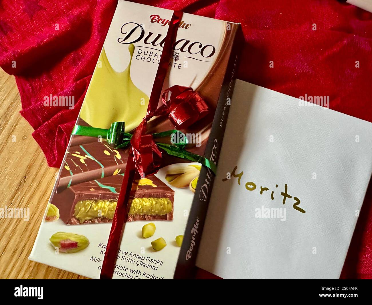 Eine verpackte Tafel Dubai Schokolade als Geschenk neben einem weißen Umschlag mit dem Namen Moritz Stockfoto
