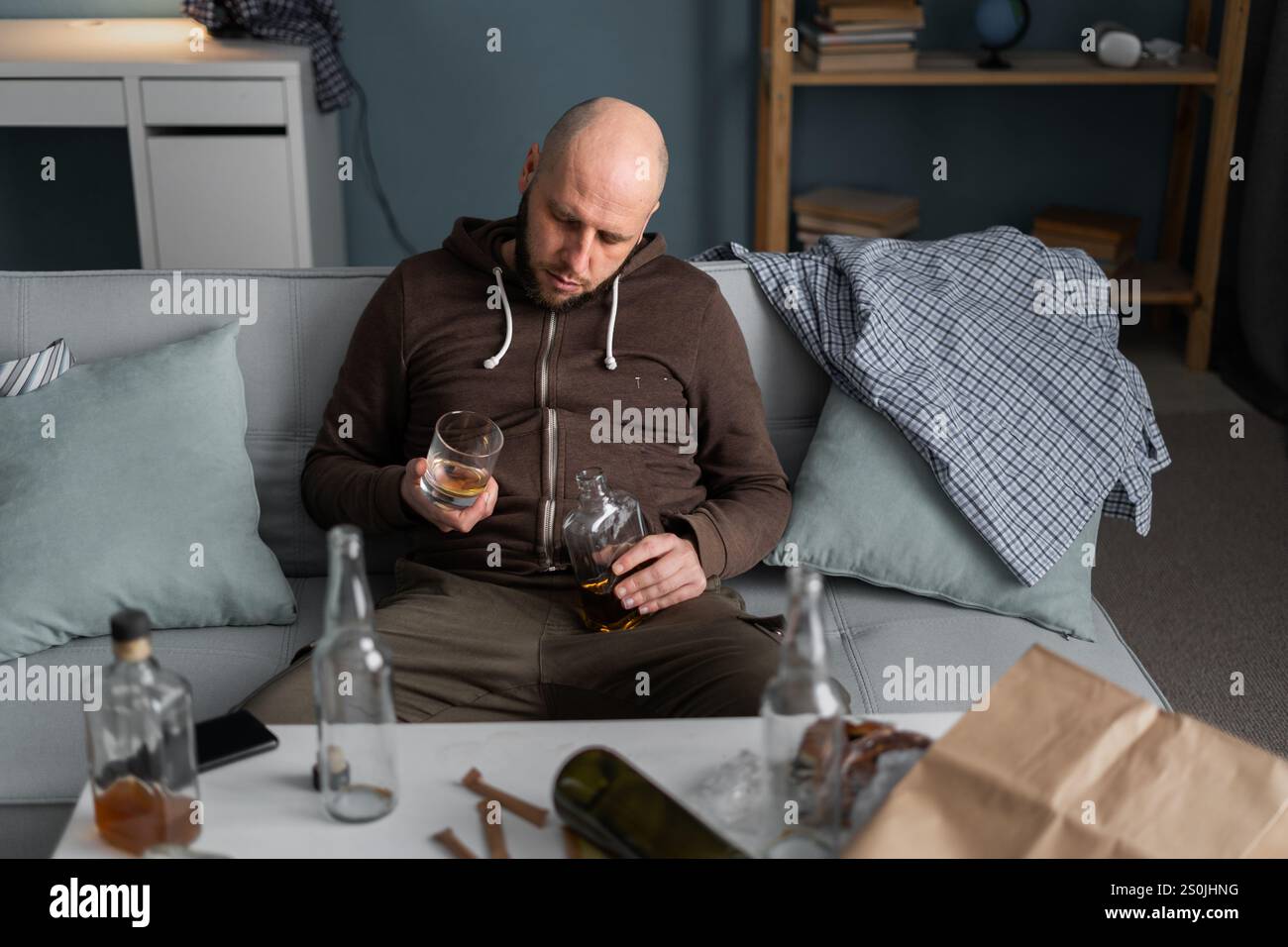 Schlafender einsamer betrunkener Mann auf Sofa mit Flasche und Glas. Das Haus ist chaotisch. Depression. Kopierbereich Stockfoto