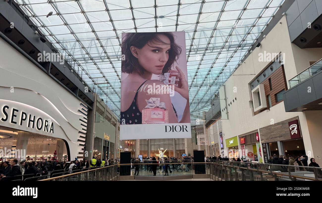 Innenblick auf das Atrium eines Einkaufszentrums mit einer großen Dior-Parfümwerbung, die von der Glasdecke abgehängt wird. Käufer sind auf dem gr Stockfoto