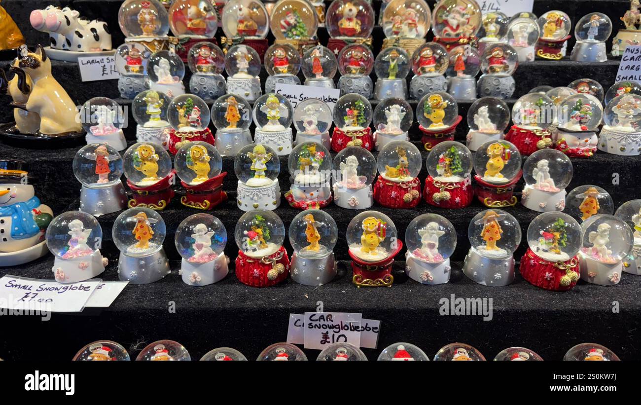 Zahlreiche kleine Schneekugeln mit verschiedenen Weihnachtsfiguren sind auf einer dunklen Oberfläche zu sehen. Die Globen sind in Reihen angeordnet, mit pric Stockfoto