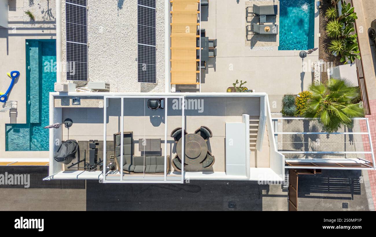 Blick aus der Vogelperspektive auf eine stilvolle Villa mit Solarpaneelen, Dachterrasse, privatem Pool, Sitzgelegenheiten im Freien und üppiger Landschaftsgestaltung in Torrevieja. Stockfoto