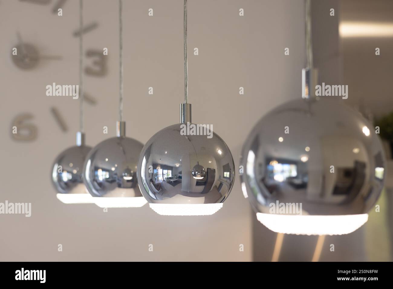 Fokussierter Blick auf schlanke Pendelleuchten aus Chrom mit reflektierenden Oberflächen, die zeitgenössisches Innendesign und Ambientebeleuchtung präsentieren. Stockfoto