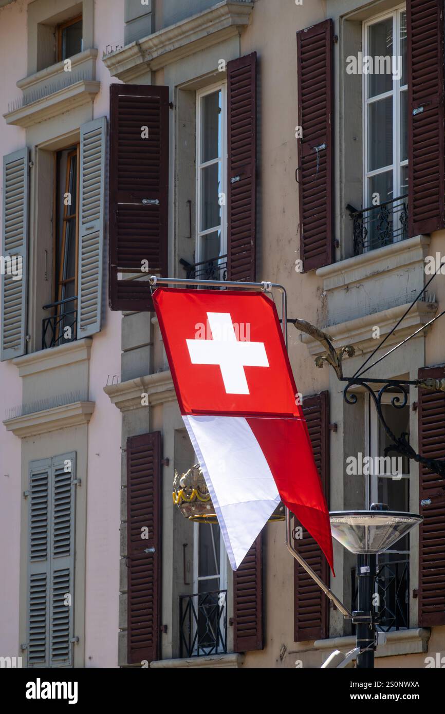 Eine rot-weiße Schweizer Flagge hängt am Gebäude in Morges. Dunkelbraune Fensterläden sind an den Fenstern. Das Gebäude hat einen klassischen europäischen Archit Stockfoto